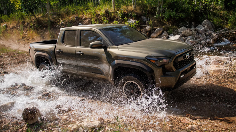2025 Toyota Tacoma driving through a shallow stream in a rugged outdoor setting, showcasing its off-road capabilities and durable design.