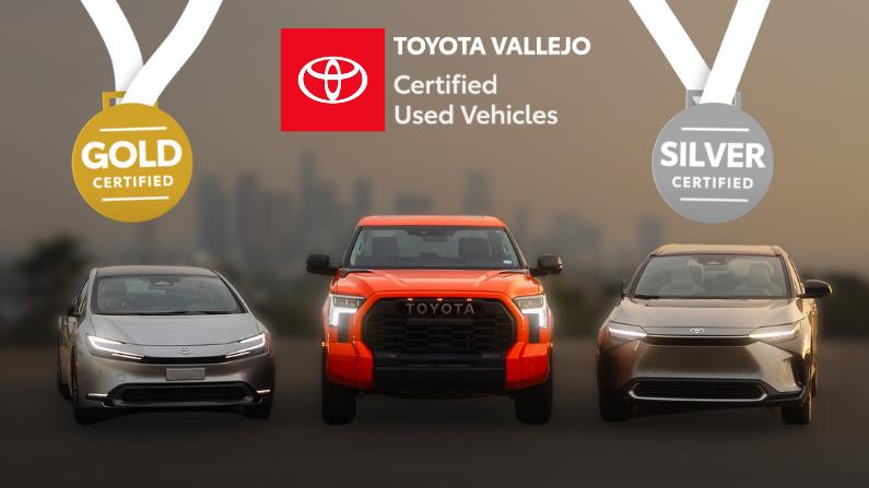 Toyota Vallejo Certified Used Vehicles promotional image featuring three Toyota vehicles: a silver sedan on the left with a gold 'Certified' medal, an orange Toyota truck in the center, and a silver SUV on the right with a silver 'Certified' medal. The background showcases a blurred city skyline at dusk